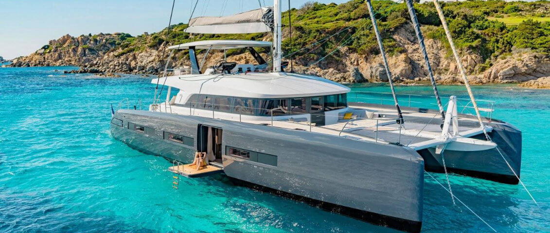 	Foto de buceo de un catamarán privado de lujo con una persona tomando el sol y otra nadando al lado.
